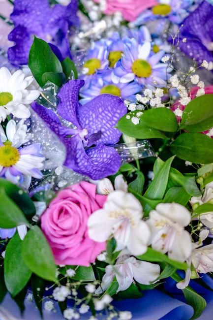 A vibrant floral arrangement featuring a mix of fresh flowers including purple orchids with patterned petals, white daisies with yellow centers, pink roses, white alstroemerias with pale pink streaks,